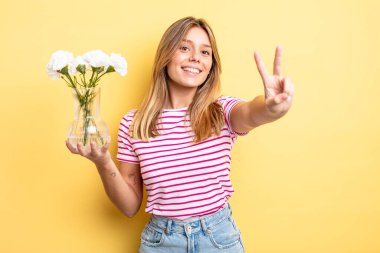Güzel sarışın kız gülümsüyor ve mutlu görünüyor, zafer ya da barış işareti yapıyor. Dekoratif çiçek konsepti