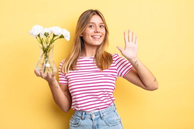Güzel sarışın kız gülümsüyor ve arkadaş canlısı görünüyor, beş numarayı gösteriyor. Dekoratif çiçek konsepti