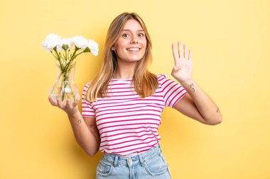 Güzel sarışın kız gülümsüyor ve arkadaş canlısı görünüyor, dört numarayı gösteriyor. Dekoratif çiçek konsepti