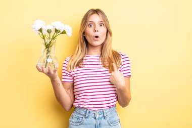 Şok olmuş ve ağzı açık, kendini işaret eden güzel sarışın bir kız. Dekoratif çiçek konsepti