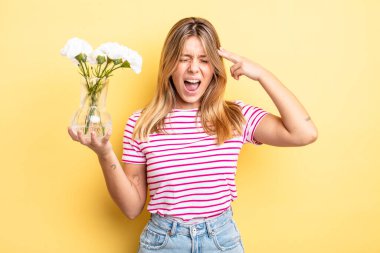 Güzel sarışın kız mutsuz ve stresli görünüyor, intihar jesti silah işareti yapıyor. Dekoratif çiçek konsepti