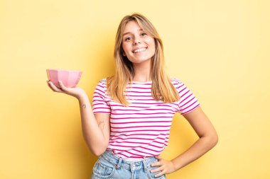 Güzel sarışın kız mutlu bir şekilde gülümsüyor, eli kalçasında ve kendinden emin. boş kase kavramı