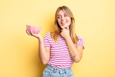 Güzel sarışın kız gülümsüyor mutlu, kendine güvenen bir yüz ifadesi ve elleri çenesinde. boş kase kavramı