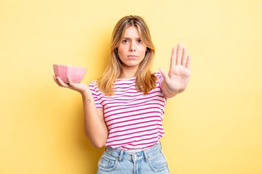 Güzel sarışın kız ciddi görünüyor. Avuç içini gösteriyor. Durma hareketi yapıyor. boş kase kavramı