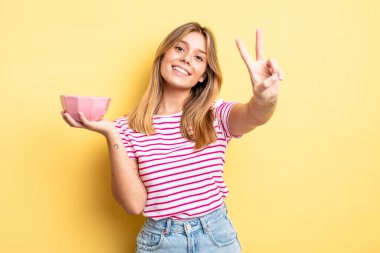 Güzel sarışın kız gülümsüyor ve mutlu görünüyor, zafer ya da barış işareti yapıyor. boş kase kavramı