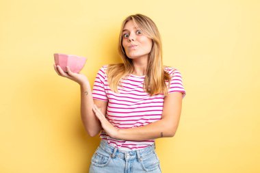 Güzel sarışın kız omuz silkiyor, kafası karışık ve kararsız. boş kase kavramı