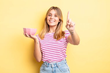 Güzel sarışın kız gururla gülümsüyor ve kendinden emin bir numara oluyor. boş kase kavramı