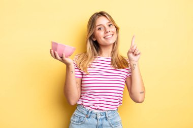 Güzel sarışın kız gülümsüyor ve arkadaş canlısı görünüyor. Bir numarayı gösteriyor. boş kase kavramı