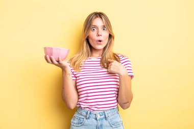 Şok olmuş ve ağzı açık, kendini işaret eden güzel sarışın bir kız. boş kase kavramı