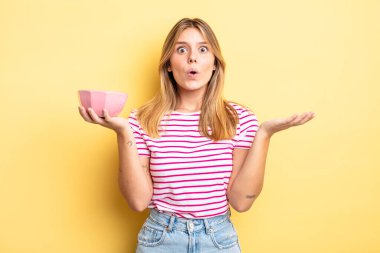 Güzel sarışın kız şaşırmış ve şok olmuş görünüyor. Çenesi düşmüş ve elinde bir nesne var. boş kase kavramı