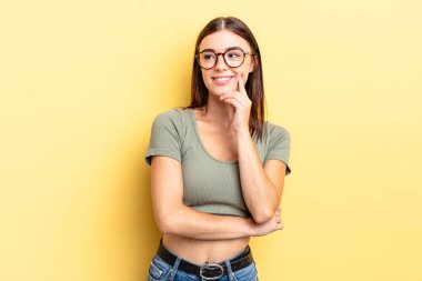 İspanyol güzel bir kadın mutlu, kendinden emin bir ifadeyle gülümsüyor. Elleri çenesinde, merak ediyor ve yan tarafa bakıyor.