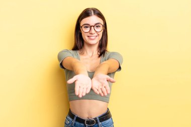 İspanyol güzel kadın mutlu bir şekilde gülümsüyor, arkadaş canlısı, kendinden emin, olumlu bakışlı, bir nesne ya da konsept sunuyor ve gösteriyor.