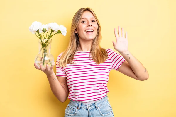 Güzel sarışın kız mutlu bir şekilde gülümsüyor, el sallıyor, hoş geldin diyor ve seni selamlıyor. Dekoratif çiçek konsepti