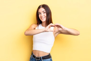 İspanyol güzel kadın gülümsüyor ve mutlu, sevimli, romantik ve aşık, iki eliyle kalbi şekillendiriyor.