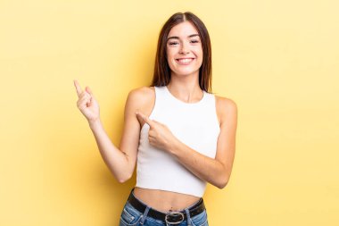 İspanyol güzel kadın mutlu bir şekilde gülümsüyor ve her iki elinle de fotokopi alanında nesne gösteriyor.