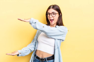 İspanyol asıllı güzel bir kadın bir objeyi iki eliyle fotokopi alanında tutuyor, bir objeyi gösteriyor, sunuyor ya da reklamını yapıyor.