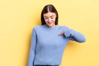 İspanyol güzel kadın neşeyle gülümsüyor, yere bakıyor ve göğsüne işaret ediyor.