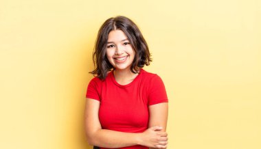 Genç ve güzel bir kız utangaç ve neşeli bir şekilde gülüyor, arkadaş canlısı ve olumlu ama güvensiz bir tavırla