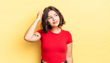 Genç güzel kız kafası karışmış ve kafası karışmış hissediyor, başını kaşıyor ve yan tarafa bakıyor.