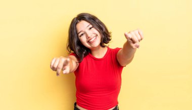 Genç ve güzel bir kız mutlu ve kendinden emin, kamerayı iki eliyle gösteriyor ve gülüyor, seni seçiyor.