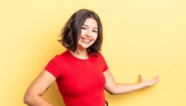 Genç güzel kız mutlu ve neşeli hissediyor, gülümsüyor ve seni selamlıyor, dostça bir jestle içeri davet ediyor.