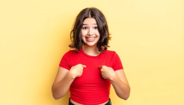 Genç, güzel bir kız mutlu, şaşırmış ve gururlu. Heyecanlı ve şaşkın bir bakışla kendini işaret ediyor.