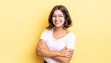 Genç ve güzel bir kız kollarını kavuşturup mutlu bir şekilde gülüyor, rahat, pozitif ve tatmin edici bir pozla.