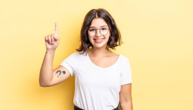 Genç ve güzel bir kız mutlu bir şekilde gülümsüyor, tek eliyle yukarıyı işaret ederek boşluğu kopyalıyor.