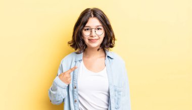 Genç ve güzel kız gururlu, kendinden emin ve mutlu görünüyor, gülümsüyor ve kendini işaret ediyor ya da bir numara işareti yapıyor.