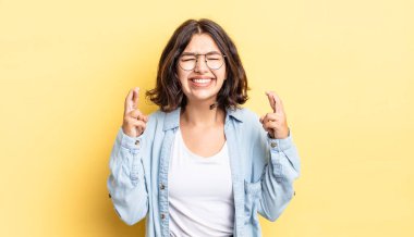 Genç ve güzel kız gülümsüyor ve endişeyle iki parmağını çapraz yapıyor, endişeli hissediyor ve iyi şanslar diliyor veya umut ediyor.