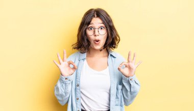 Genç, güzel bir kız şok olmuş, şaşırmış ve şaşırmış hissediyor. İki eliyle de onay işareti yapıyor.