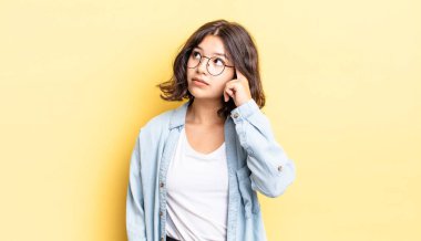 Yoğunlaşmış bakışları olan genç ve güzel bir kız şüpheli bir ifadeyle yukarı ve yana bakıyor.