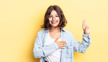 Genç, güzel bir kız mutlu, kendinden emin ve güvenilir görünüyor, gülümsüyor ve zafer işareti gösteriyor, olumlu bir tavırla.