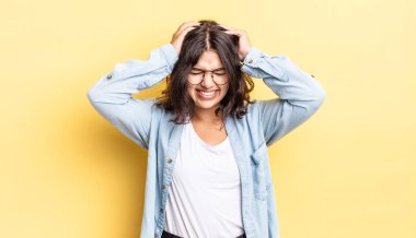 Genç ve güzel bir kız stresli ve hayal kırıklığına uğramış hissediyor, ellerinizi havaya kaldırıyor, yorgun, mutsuz ve migren ağrısı çekiyor.