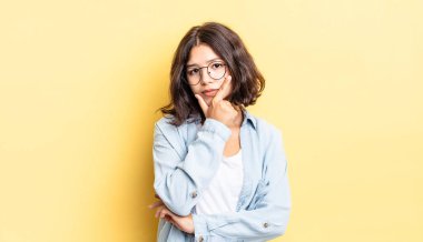 Genç ve güzel bir kız ciddi, düşünceli ve güvensiz görünüyor, bir kolu çapraz ve çene üzerinde, seçenekleri tartıyor.