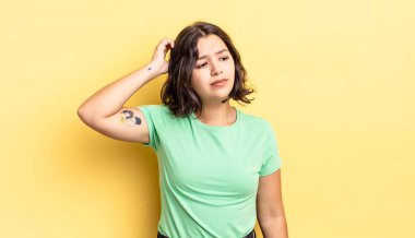 Genç güzel kız kafası karışmış ve kafası karışmış hissediyor, başını kaşıyor ve yan tarafa bakıyor.