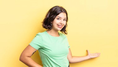 Genç güzel kız mutlu ve neşeli hissediyor, gülümsüyor ve seni selamlıyor, dostça bir jestle içeri davet ediyor.