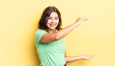 Genç güzel kız gülümsüyor, mutlu, pozitif ve tatmin olmuş hissediyor, fotokopi alanında nesne ya da konsept tutuyor ya da gösteriyor