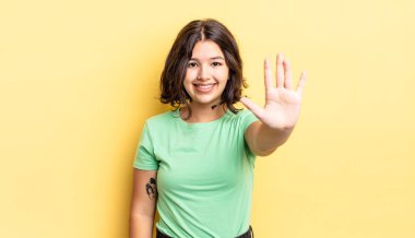 Genç ve güzel bir kız gülümsüyor ve arkadaş canlısı görünüyor, 5 ya da 5 numarayı gösteriyor, elleri önde, geriye doğru sayıyor.