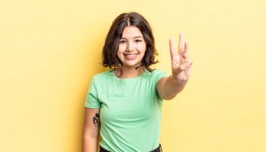 Genç, güzel bir kız gülümsüyor ve arkadaş canlısı görünüyor. Üç ya da üç numarayı gösteriyor. Elleri önde, geri sayıyor.