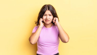 Genç, güzel bir kız sinirli, stresli ve sinirli görünüyor, iki kulağını da sağır edici bir ses, ses ya da yüksek sesle kapatıyor.