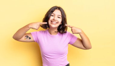 Genç, güzel bir kız, kendine güvenerek gülümsüyor. Geniş bir gülümseme, pozitif, rahat, tatmin olmuş bir tavır.