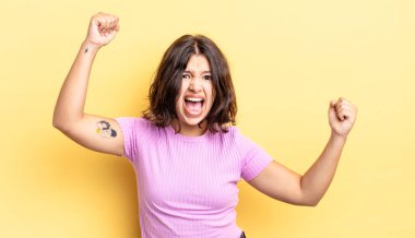 Genç ve güzel bir kız muzaffer bir şekilde bağırıyor. Heyecanlı, mutlu ve şaşırmış görünüyor. Kutlama yapıyor.