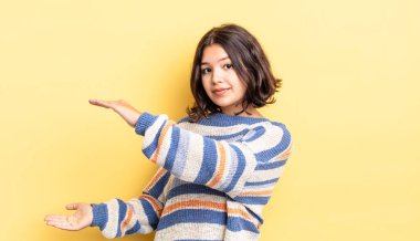 Genç, güzel bir kız iki eliyle bir objeyi tutuyor fotokopi alanında, bir nesneyi gösteriyor, sunuyor ya da reklamını yapıyor.