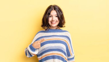 Genç ve güzel kız gururlu, kendinden emin ve mutlu görünüyor, gülümsüyor ve kendini işaret ediyor ya da bir numara işareti yapıyor.