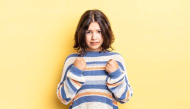 Genç ve güzel bir kız kendinden emin, sinirli, güçlü ve agresif görünüyor. Yumrukları boks pozisyonunda dövüşmeye hazır.