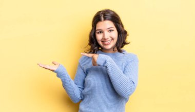 Genç ve güzel bir kız neşeyle gülümsüyor ve bir objeyi gösteren ya da reklamını yapan avuç içindeki kopyalama alanını işaret ediyor.