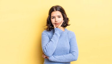 Genç ve güzel bir kız ciddi, düşünceli ve güvensiz görünüyor, bir kolu çapraz ve çene üzerinde, seçenekleri tartıyor.