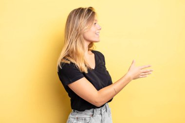 Sarışın, güzel bir kadın gülümsüyor, seni selamlıyor ve başarılı bir anlaşma için el sıkışmayı teklif ediyor, işbirliği konsepti.