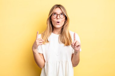 Şok olmuş, şaşkın ve ağzı açık, iki eliyle uzayı gösteren güzel sarışın bir kadın.